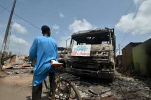 A cyclist reads a sign on a burnt truck calling for violence to stop in the market of Toumodi. By SIA KAMBOU (AFP)