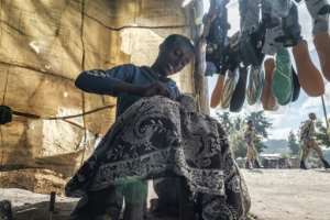 A cobbler in Korem, a town north of Alamata, repairs a shoe as soldiers of the Amhara special forces walk by. By EDUARDO SOTERAS (AFP)