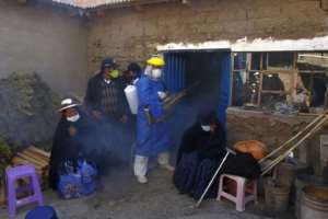 A funerary employee in protective gear disinfects the home of a COVID-19 victim as relatives mourn outside, in the remote Aymara highland village of Acora in Peru. By Carlos MAMANI (AFP)