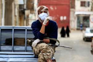 A fighter loyal to the Huthi rebels keeps guard as volunteers take measures to prevent the spread of COVID-19 in Yemen's capital Sanaa. By MOHAMMED HUWAIS (AFP)