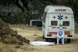 A health worker wearing protective gear sits on an ambulance next to the body of a COVID-19 victim before burial at a graveyard in New Delhi. By SAJJAD HUSSAIN (AFP)