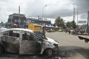 A policeman gestures next to a car in Abidjan's Cocody district that was torched in anti-Ouattara protests on October 19. By SIA KAMBOU (AFP)