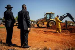 A relative and a pastor stand by as a mechanical digger moves in to cover the grave. By Michele Spatari (AFP)