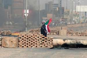 A Sudanese demonstrator carrying a national flag walks by roadblocks set up by protesters in Khartoum. By - (AFP)