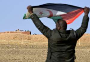 A Sahrawi, in February 2017, holds up a Polisario flag under the watchful eye of Moroccan soldiers guarding an observation post on the 2,700-kilometer-long (1,700-mile) wall that Rabat built to defend its control of the disputed Occidental Sahara.  By STRINGER (AFP / Archive)