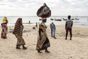 A woman carries her belongings off a boat as she arrives at Paquitequete beach in Pemba after fleeing Palma by boat with forty nine other people. By JOHN WESSELS (AFP)