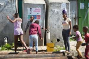 A woman fills a bucket from a communal tap as children play. By RODGER BOSCH (AFP)