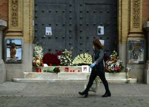 A woman walks past a church in Seville, adorned with flowers and candles left by the faithful after Easter processions were cancelled. By CRISTINA QUICLER (AFP)
