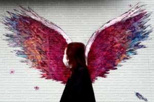 A woman wearing a face mask amid concerns over COVID-19 walks past a graffiti of wings in Tokyo. By Behrouz MEHRI (AFP)