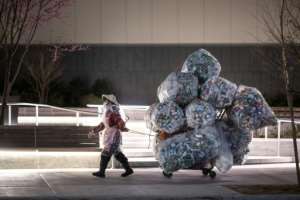 A woman wearing a face mask and a plastic bag pulls a cart loaded with bags of recyclables through the streets of Lower Manhattan. By Johannes EISELE (AFP)