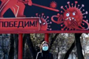 A woman wearing a face mask walks past a sign depicting a virus in Minsk. By Sergei GAPON (AFP)