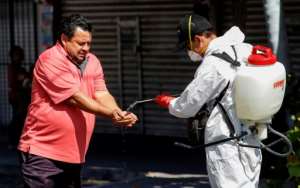 A worker wearing a protective suit sprays disinfectant on a man's hands during a campaign to sanitize public spaces in Guadalajara, Mexico. By ULISES RUIZ (AFP)