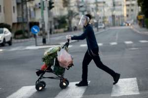 An ultra-Orthodox Jewish youth wearing a protective plastic mask crosses a street with his shopping in the Israeli city of Bnei Brak near Tel Aviv. By MENAHEM KAHANA (AFP)