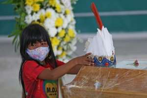 An indigenous girl from Parque das Tribos community leaves a headdress on the coffin of Chief Messias, 53, of the Kokama tribe who died of COVID-19, in Manaus, Brazil. By MICHAEL DANTAS (AFP)