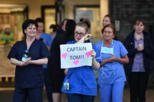 An NHS staff member wipes her eyes as she holds a sign to thank British veteran Captain Tom Moore, who raised over 13 million pounds for the NHS, as they take part in a national