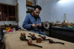 Anis Bouchnak and some of the wood pipes he has carved; the Bouchnak family workshop was established half a century ago. By FETHI BELAID (AFP)