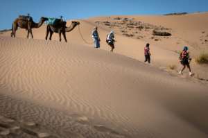 Competitors run past a camel caravan during the 35th edition of the Marathon des Sables in the southern Moroccan Sahara on October 8, 2021. Morocco depends heavily on visitors to its coastal resorts and historic inland cities. By JEAN-PHILIPPE KSIAZEK (AFP/File)