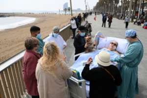 Friends, neighbours and medical personnel surround COVID-19 patient Marta Pascual, 72, as she gets some fresh air at the Barceloneta beach esplanade in Barcelona, Spain. By LLUIS GENE (AFP)