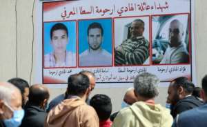 Libyans gather by a wall poster depicting victims from one family during a funeral procession for 12 bodies that were identified from mass graves found in Tarhuna town. By Mahmud Turkia (AFP)