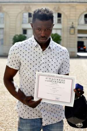 Mamoudou Gassama from Mali displays a certificate of courage and dedication signed by Paris Police Prefect Michel Delpuech for saving the life of a four-year-old child dangling from a Paris appartment balcony.  By Thibault Camus (POOL/AFP)