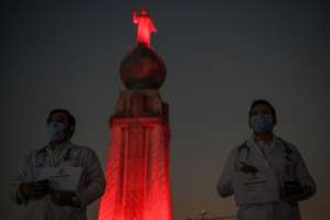 Medical personnel in San Salvador stand in front of the monument to the Divine Saviour of the World which was lit up as a tribute to healthcare workers. By Yuri CORTEZ (AFP)