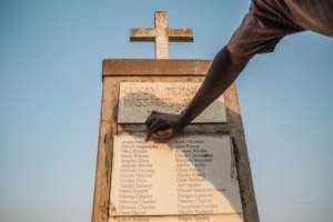 Olanyia Mohammed, 38, escaped a massacre in his village but lost 15 members of his family. He points at his parents names etched on a memorial. By Sumy Sadurni (AFP)