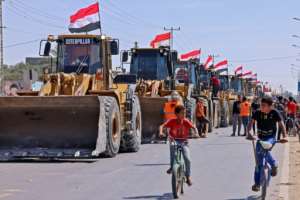Palestinian boys cycle past a convoy of bulldozers provided by Egypt arriving at the Palestinian side of the Rafah border crossing between Egypt and the Palestinian Gaza Strip enclave on June 4, 2021. By SAID KHATIB (AFP/File)