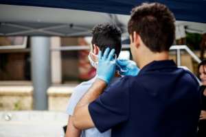 Paramedic Albrae Cilliers (L) ties a protective face mask on an incoming visitor. By Michele Spatari (AFP)