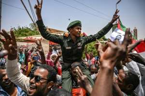 Sudanese protestors shout slogans as they carry a soldier flashing the victory sign outside the army complex.  By OZAN KOSE (AFP)